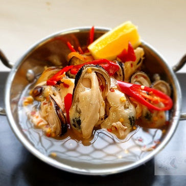 Stir-fried seafood dish with vegetables in a metal dish on a dark surface.