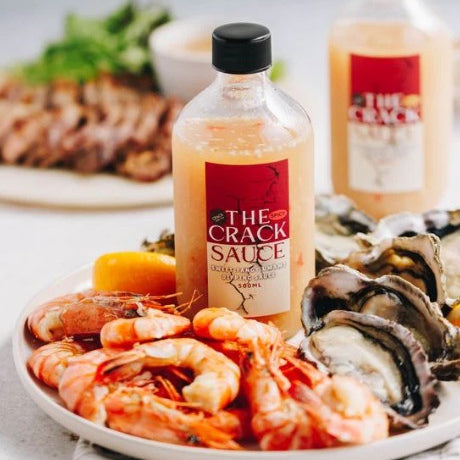 Bottle of 'The Crack Sauce' on a plate with seafood and other food items.