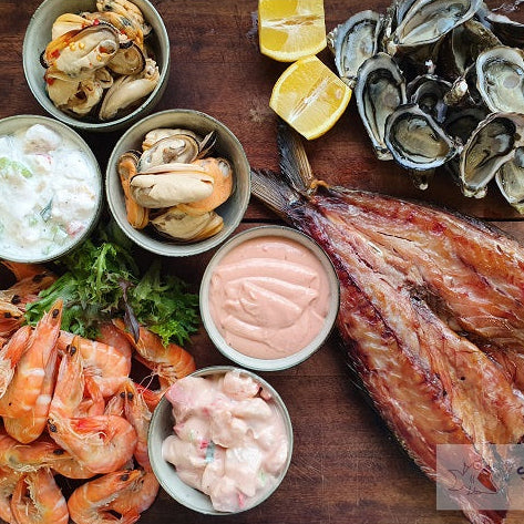 Assorted seafood including prawns, oysters, and fish on a wooden board with sauces.