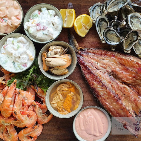 Assorted seafood including oysters, shrimp, and fish on a wooden board with 'Seafood Bazaar' branding.
