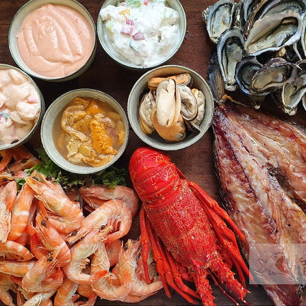 Assorted seafood including oysters, shrimp, and a lobster on a wooden surface with side dishes.