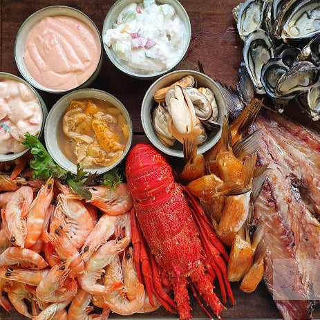 Assorted seafood including shrimp, lobster, and oysters with side dishes on a wooden surface.