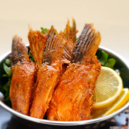 Fried fish served in a decorative bowl with lemon wedges on a dark surface.
